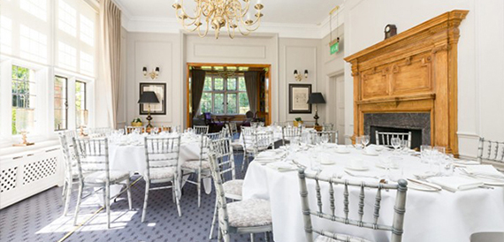 Dining room with round tables, silver chiavari chairs and a large oak fireplace.