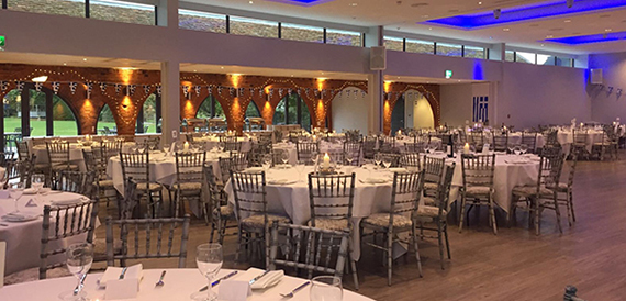 Event hall with round tables, silver chiavari chairs and blue mood lighting.