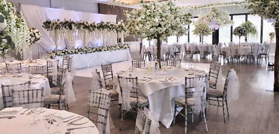 Wedding reception with round tables, blossom tree centrepieces and draped ceiling fabric.
