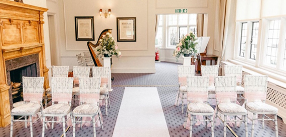 Wedding ceremony room with rows of chairs, a harp and a white aisle runner.
