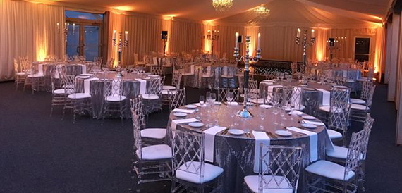 Marquee dinner set-up with round tables, clear chiavari chairs and tall candelabras