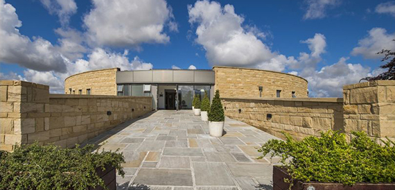 Curved stone clubhouse entrance with a paved path under a blue sky