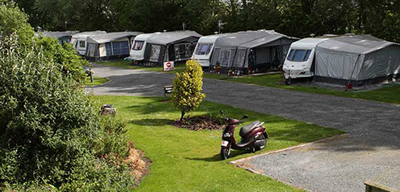Row of touring caravans with awnings parked along a grassy caravan park