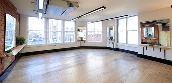 Empty studio space with a wooden floor, wall mirrors and large windows