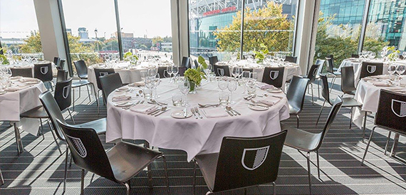 Round dining tables set with glassware, overlooking the football stadium through glass windows
