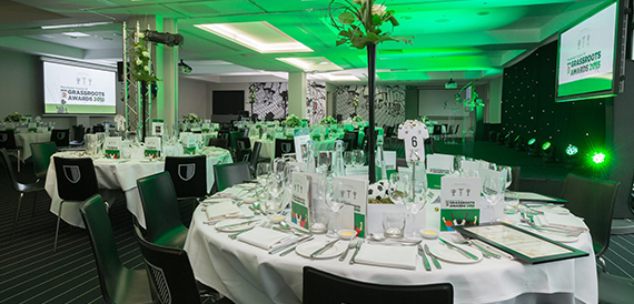 Awards dinner set-up with green lighting, round tables and screens showing an awards ceremony