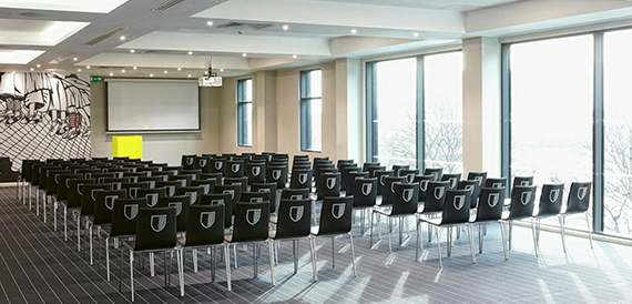 Theatre-style conference seating facing a projector screen beneath a graphic wall mural