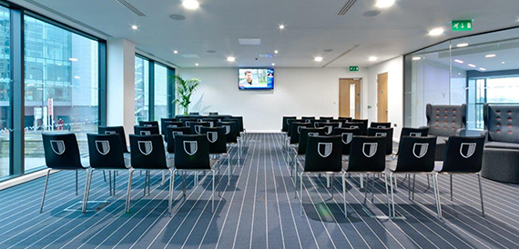 Meeting space with theatre-style seating facing a wall-mounted screen and glass windows