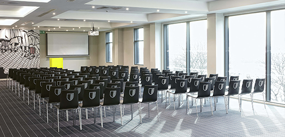 Conference room set theatre-style with rows of crested chairs facing a projector screen