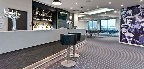 Bar area with beer taps, bottle display and black leather stools beside a large mural