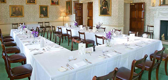 Dining room with a long table set formally beneath portrait paintings