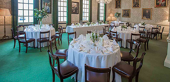 Elegant dining room with tables set formally beneath portrait paintings
