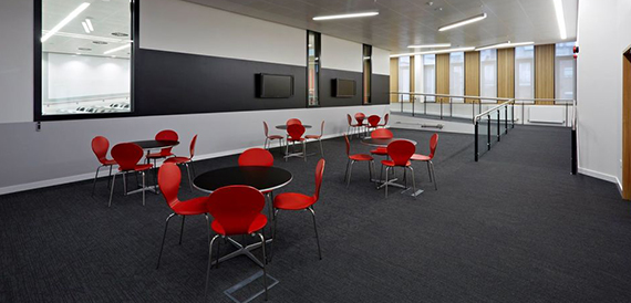 Breakout area with red chairs and round tables on dark carpet