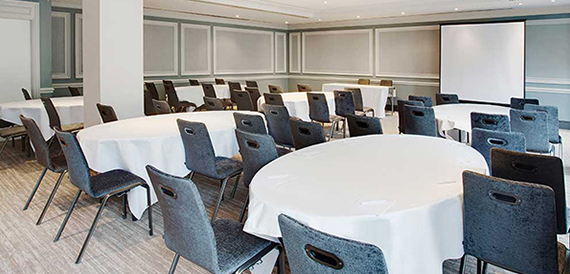Cabaret-style round tables with white cloths facing a projector screen