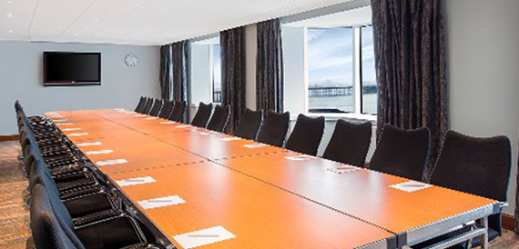 Long boardroom table with a wall screen and a view of the pier