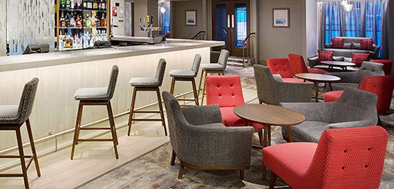 Hotel bar with stools at the counter and red and grey lounge armchairs