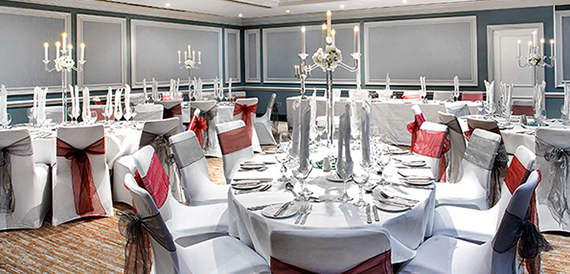 Formal dining room with round tables, red chair sashes and candelabra centrepieces