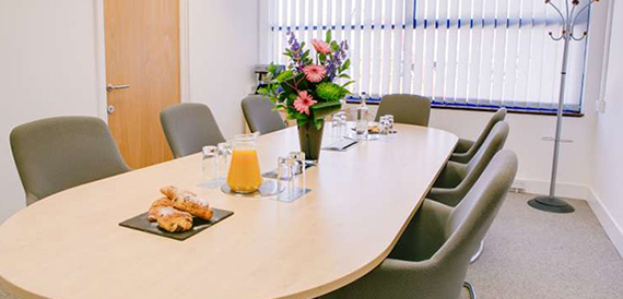 Small oval meeting table set with pastries, orange juice and flowers