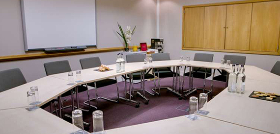 U-shaped meeting table set with water and biscuits beneath a whiteboard