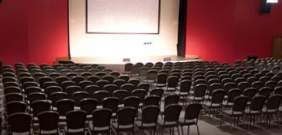 Rows of theatre seating facing a large screen against red walls