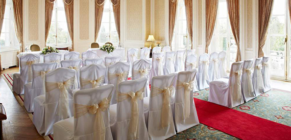 Wedding ceremony room with white chair covers, gold sashes and a red aisle carpet
