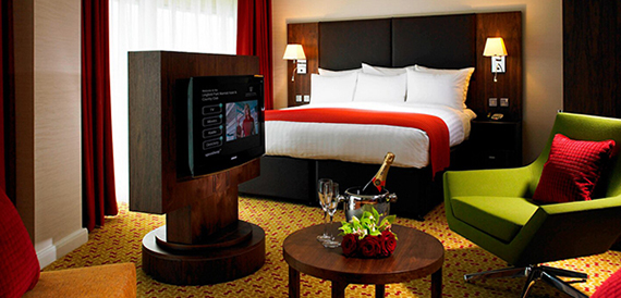 Hotel bedroom with a red bedspread, green accent chair and champagne set out