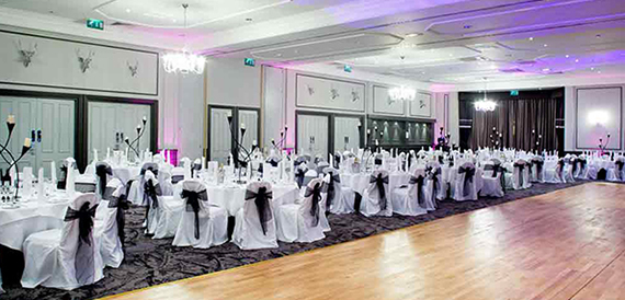 Ballroom set for a wedding with white chair covers, black sashes and a dance floor.