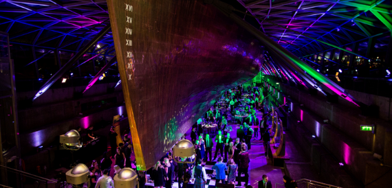 Guests mingling beneath the hull with green and pink event lighting