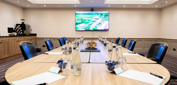 Round boardroom table with blue chairs and an estate view on screen