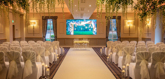 Wedding aisle lined with cream chair covers beneath a greenery arch