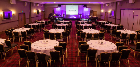 Banquet room set with round tables beneath pink and purple lighting