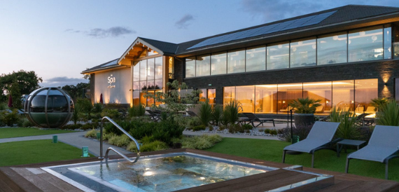 Carden Park's spa building glowing at dusk beside an outdoor pool