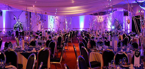 Evening event space decorated with purple lighting, fairy lights and round dinner tables