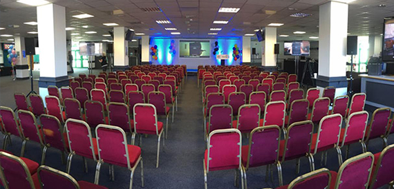 Exhibition hall set theatre-style with red chairs and a lit stage