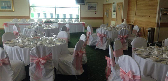 Wedding breakfast room with pink organza chair sashes and a top table.