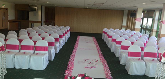 Wedding ceremony room with rows of white chairs and a pink aisle runner.