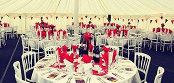 Marquee dining tables set with red napkins, wine bottles and bunting.