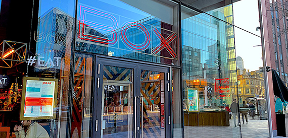 BOX Deansgate's illuminated shopfront signage on a city centre street