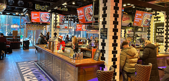 Pizza counter where customers queue beneath screens showing menus