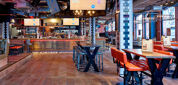 Bar area with wall-mounted screens, tall tables and orange stools