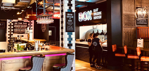 Staff serving food at a counter beneath neon 'Box' signage