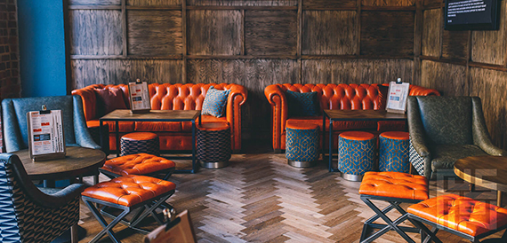 Lounge with orange chesterfield sofas and patterned stools on herringbone flooring