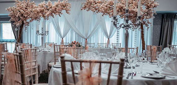 Wedding reception tables under blossom trees with a silver candelabra centrepiece.