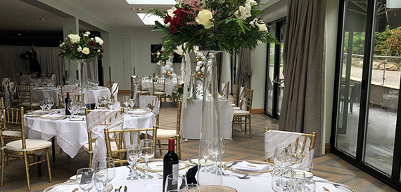 Wedding dining room with tall floral centrepieces and gold chiavari chairs.