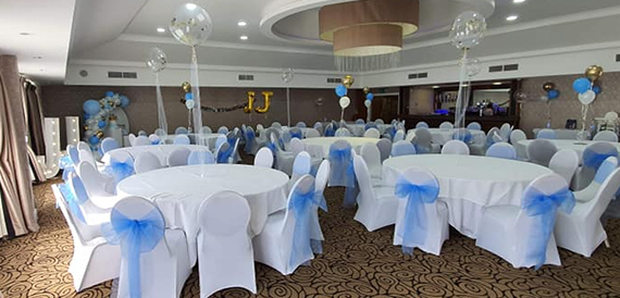 Function room set for a party with white chair covers and blue sashes.