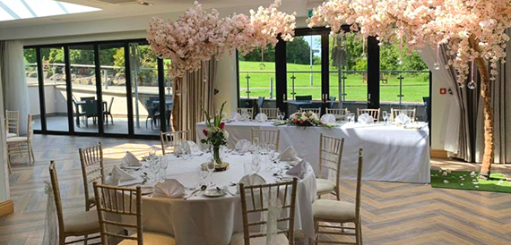 Wedding breakfast room with a top table, gold chiavari chairs and blossom trees.