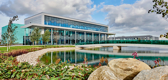 Exterior of the glass-fronted building beside a landscaped lake.