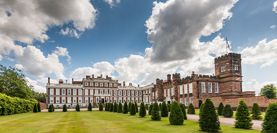 Stately home exterior with a clock tower and manicured topiary lawn