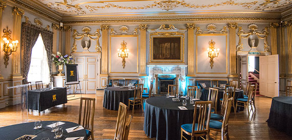 Gilded state room set with round tables beneath an ornate ceiling