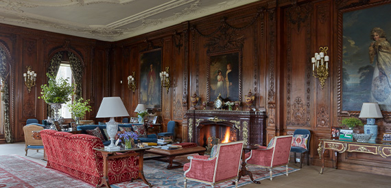 Wood-panelled drawing room with red sofas and a lit fireplace